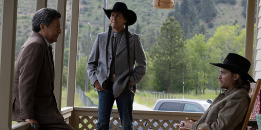 A large image of three men on a porch. A Native American man with his hair in two long black braids is wearing a bolo tie and sport jack in the center glances slightly to his left at at another Native American man wearing a suit and seated on a porch rail. To their right is a white man sporting a cowboy hat and seated in a rocking chair.