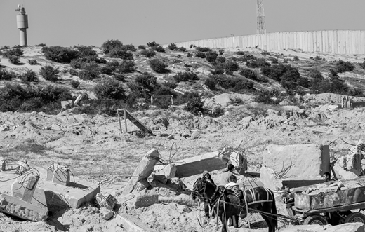 In the shadow of a surveillance tower, young boys salvage concrete and stone from an area destroyed by Israeli missile fire near the Erez checkpoint, at the northern edge of the Gaza Strip. (2012, photo by the author)
