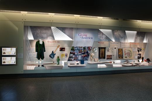 The National Museum of American History’s Giving in America exhibit as seen in 2018. The framework for the section on the right side of the case remains constant, though objects in it rotate. The section on the left changes annually around a particular theme and features Giving Pledge letters related to the theme. (National Museum of American History)